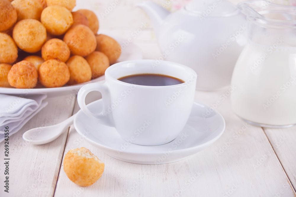 Cup of coffee with small balls of freshly baked homemade cottage cheese doughnuts in a plate on a background.