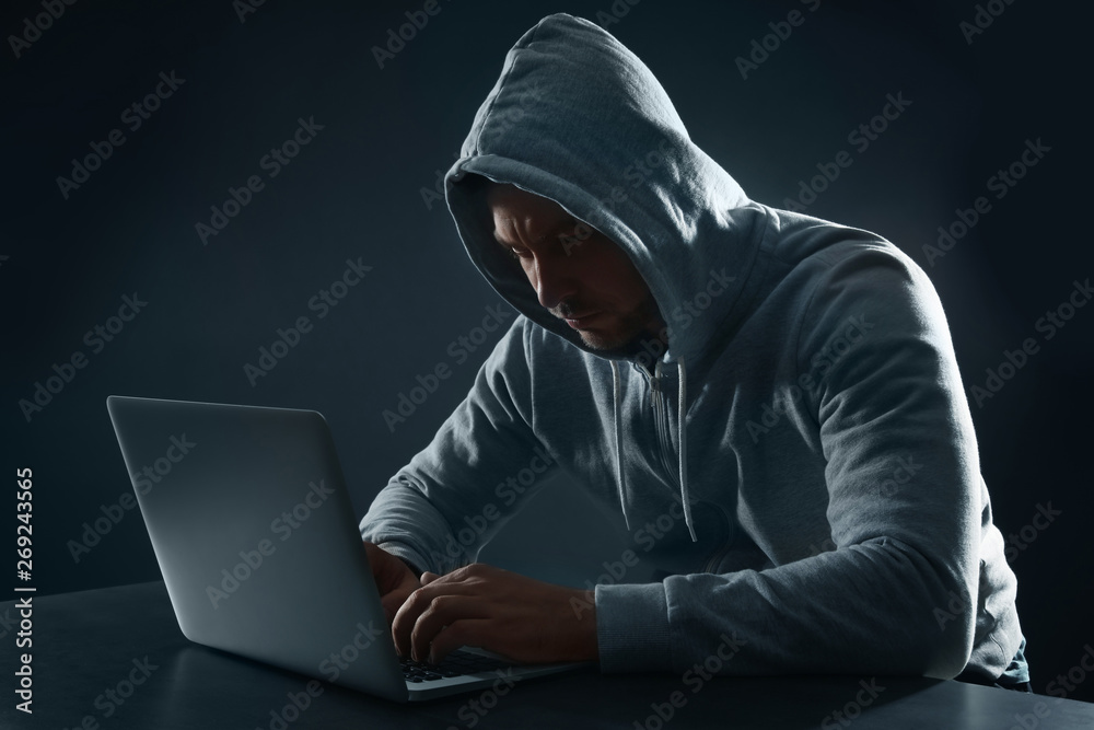 Man using laptop at table on dark background. Criminal activity Man using laptop at table on dark background. Criminal activity