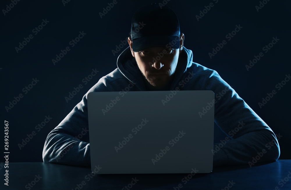 Man using laptop at table on dark background. Criminal activity Man using laptop at table on dark background. Criminal activity