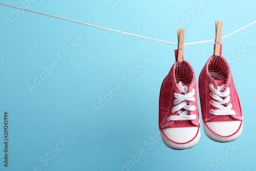 Cute small shoes hanging on washing line against color background, space for text. Baby accessories photo