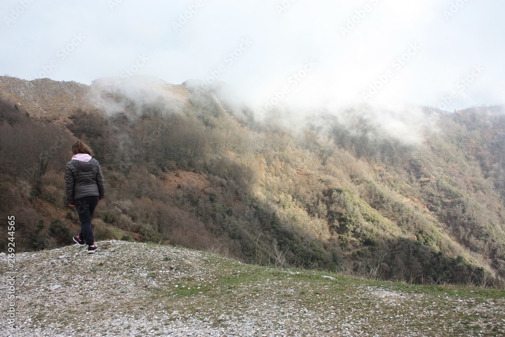 girl walks alone in the mist and fog along the paths of the Apuan Alps in Tuscany