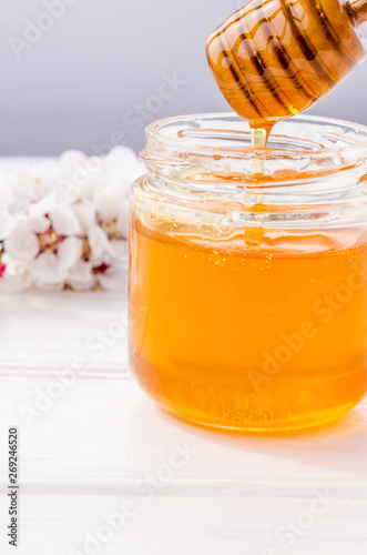 Honey flows beautifully from a wooden honey spoon into a glass jar