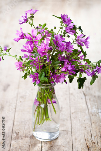 Wild violet flowers in glass bottle on rustic wooden table.
