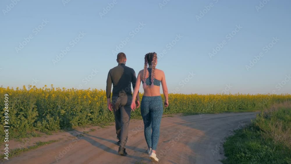 sports leisure, young couple girl and boy with kanekalon braids and athletic body walking in blooming rapeseed field against blue clear sky sports leisure, young couple girl and boy with kanekalon braids and athletic body walking in blooming rapeseed field against blue clear sky