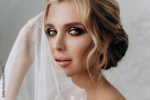 Bride with a beautiful hairstyle. Model blonde in a wedding dress in white interior