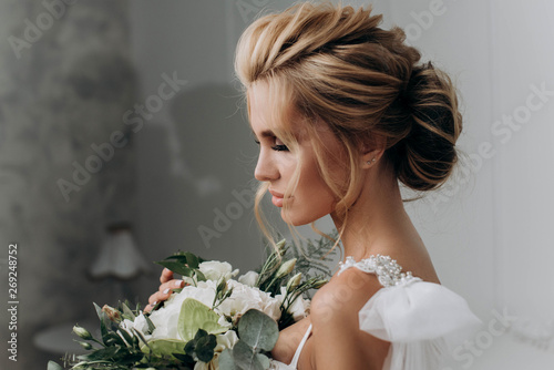 Bride with a beautiful hairstyle. Model blonde in a wedding dress in white interior