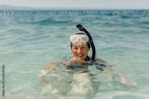 Cheerful woman wearing diving mask and snorkel smiling in water. Snorkeling - happy female diver enjoying being in sea.