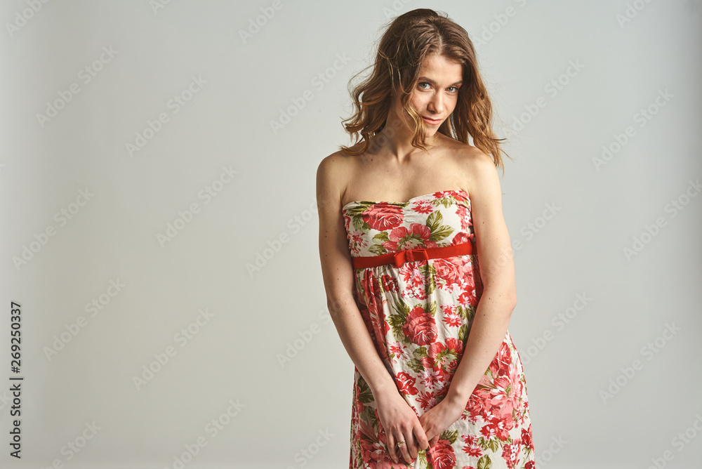 young, sympathetic, mysterious, spontaneous, seksualana, European light girl with loose hair in a light colored dress colors, smiles. On the light gray background young, sympathetic, mysterious, spontaneous, seksualana, European light girl with loose hair in a light colored dress colors, smiles. On the light gray background