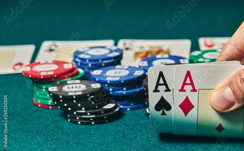 close-up of two aces held in one hand on the green game mat on the right side of the image to leave room for editing, other cards and poker chips are on the mat