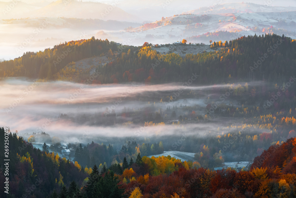 Beautiful autumn rural scenery. Landscape with amazing mountains, fields and forests covered with morning fog. The lawn is enlightened by the sun rays. Touristic place Carpathians, Ukraine, Europe.
