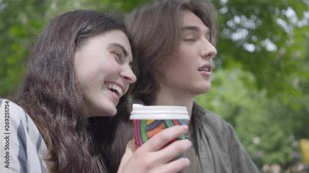 Portrait adorable young happy couple in casual clothes spending time together in the park, having a date. The students drinking coffee, girl sharing her beverage with boyfriend, but he does not like Portrait adorable young happy couple in casual clothes spending time together in the park, having a date. The students drinking coffee, girl sharing her beverage with boyfriend, but he does not like