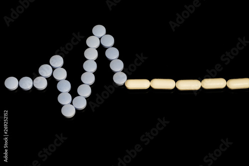 Medicines white, round heart shaped pills on black background. Tablets in the form of a line of a heart rhythm on a black background. Cardiogram of heart from pills