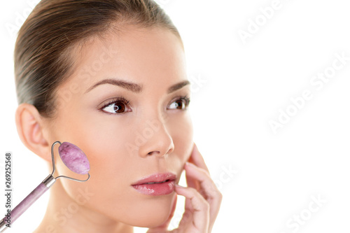 Face jade roller massage Asian beauty woman massaging cheeks with pink rose quartz tool.