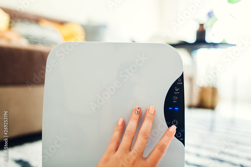 Woman turns dehumidifier on using touch panel at home. Modern airdryer device for cleaning air photo