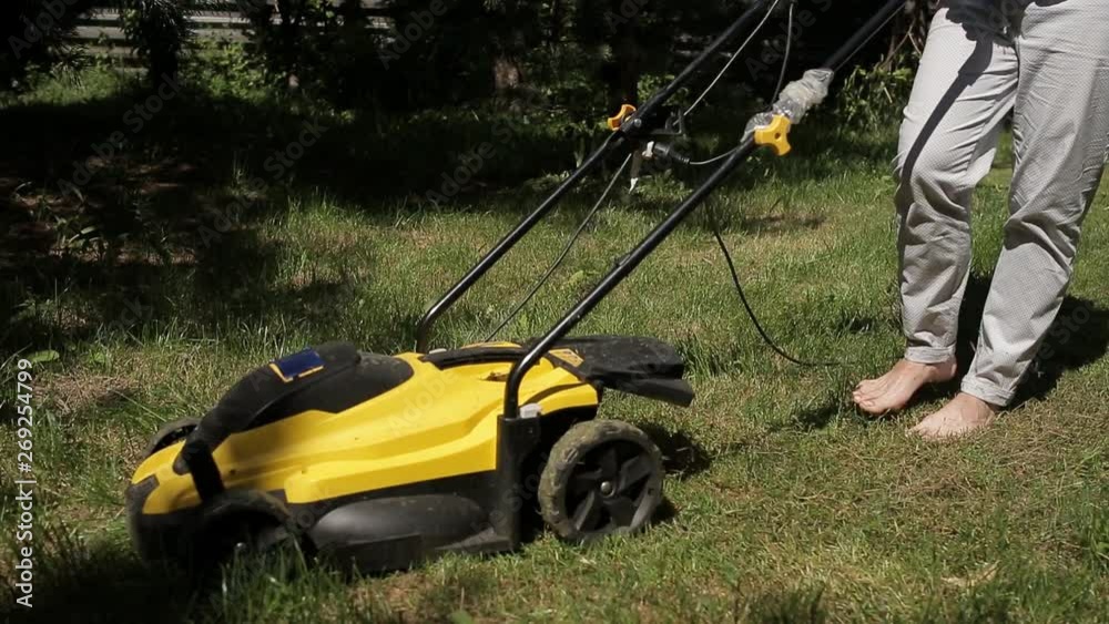 the girl is mowing an uneven lawn with yellow lawnmower barefoot Stock