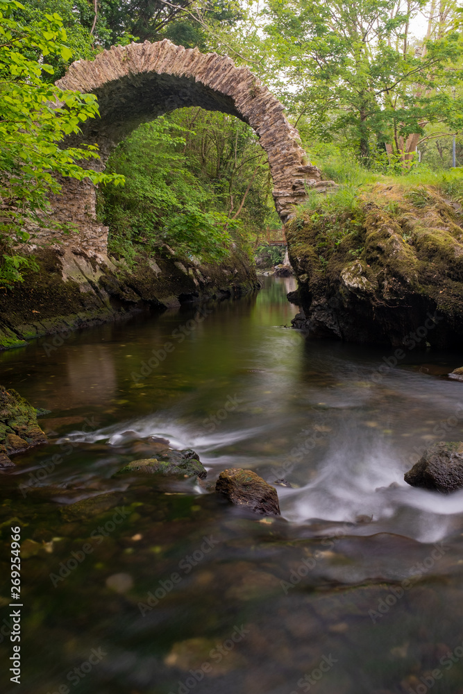 A view of the ancient Cromwell Bridge in Kenmare, County Kerry, Ireland, taken from upstream on a long exposure to smooth out the water, nobody in the image A view of the ancient Cromwell Bridge in Kenmare, County Kerry, Ireland, taken from upstream on a long exposure to smooth out the water, nobody in the image