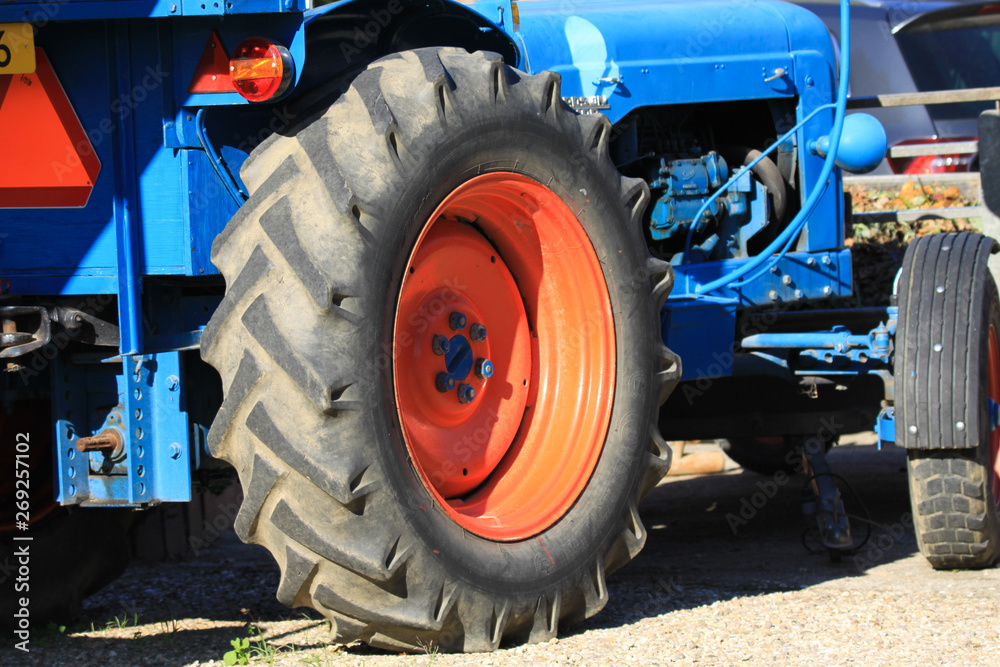 Close up of black wheels tire with deep sufficient tread and engine of antique old tractor with red rim and blue nuts on a farm in Netherland Close up of black wheels tire with deep sufficient tread and engine of antique old tractor with red rim and blue nuts on a farm in Netherland