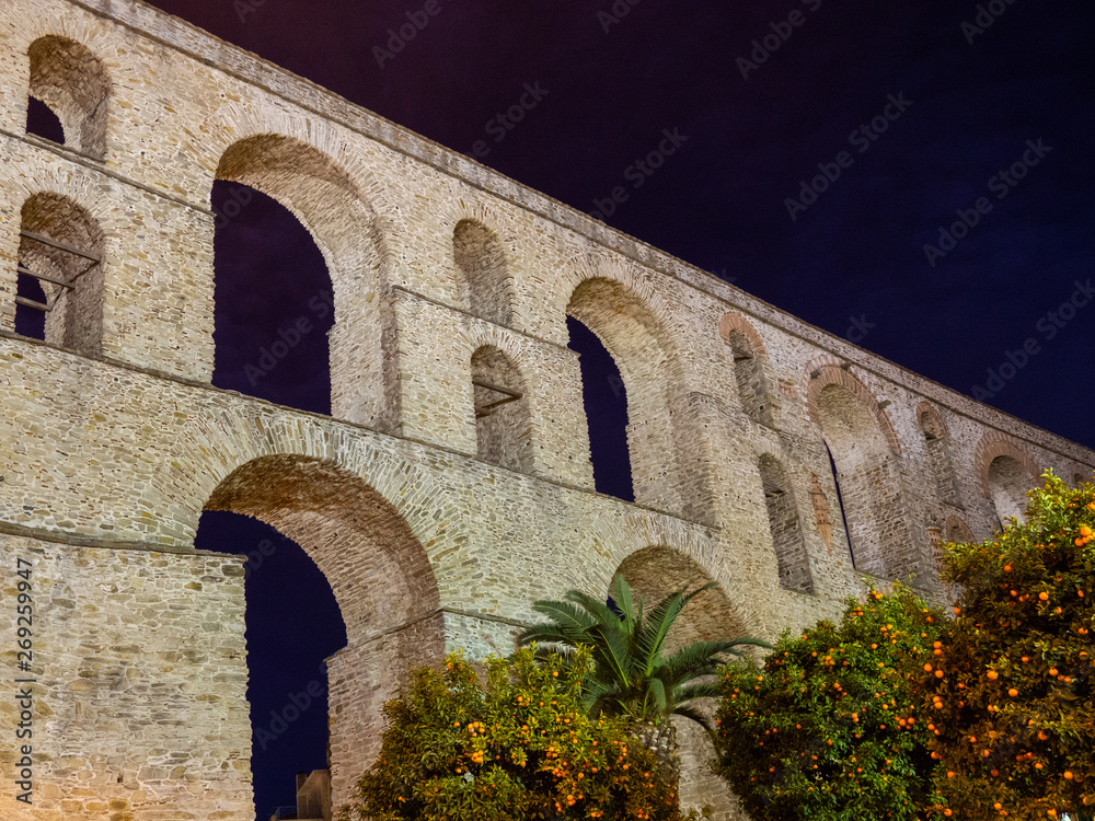 Ancient Roman aqueduct, orange trees and palms in front of it - night shot - Kavala, Greece