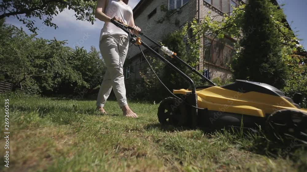 the girl is mowing an uneven lawn with yellow lawnmower barefoot Stock