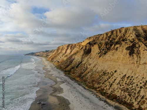 Картината върху платно Aerial view of pacific coastline with yellow sandstone cliffs and waves rushing the beach during sunset