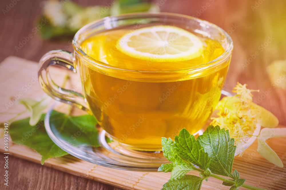 A cup with fragrant lime tea, standing on a wooden table, in the rays of sunlight. A cup with fragrant lime tea, standing on a wooden table, in the rays of sunlight.