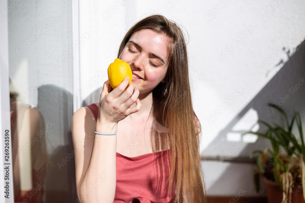 Young happy pretty female in casual summer dress sitting on terrace and covering eyes with ripe lemons Young happy pretty female in casual summer dress sitting on terrace and covering eyes with ripe lemons