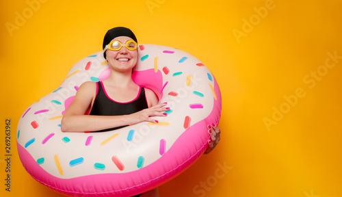 Photo of happy girl in swimming goggles, swimsuit with donut life buoy on empty orange background © Sergey