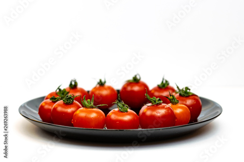 Tomatoes in a black plate isolated on white background. Composition of red tomatoes on a white background. Place for text