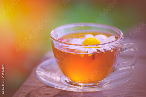 A cup of fragrant chamomile tea, in the rays of the evening beautiful sunset.