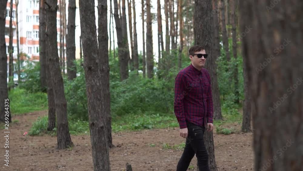 Young man walking on path in forest, summer day. Portrait of young man in casual clothes, walking along path in quiet autumn park Young man walking on path in forest, summer day. Portrait of young man in casual clothes, walking along path in quiet autumn park