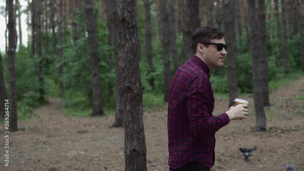 Man drinking coffee in woods. Casual man enjoying hot drink in paper cup strolling in sunny forest Man drinking coffee in woods. Casual man enjoying hot drink in paper cup strolling in sunny forest