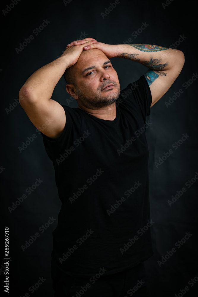 Emotions, a man in a black t-shirt looks hopefully at the camera with his hands folded on his head, isolated on a black background. Emotions, a man in a black t-shirt looks hopefully at the camera with his hands folded on his head, isolated on a black background.