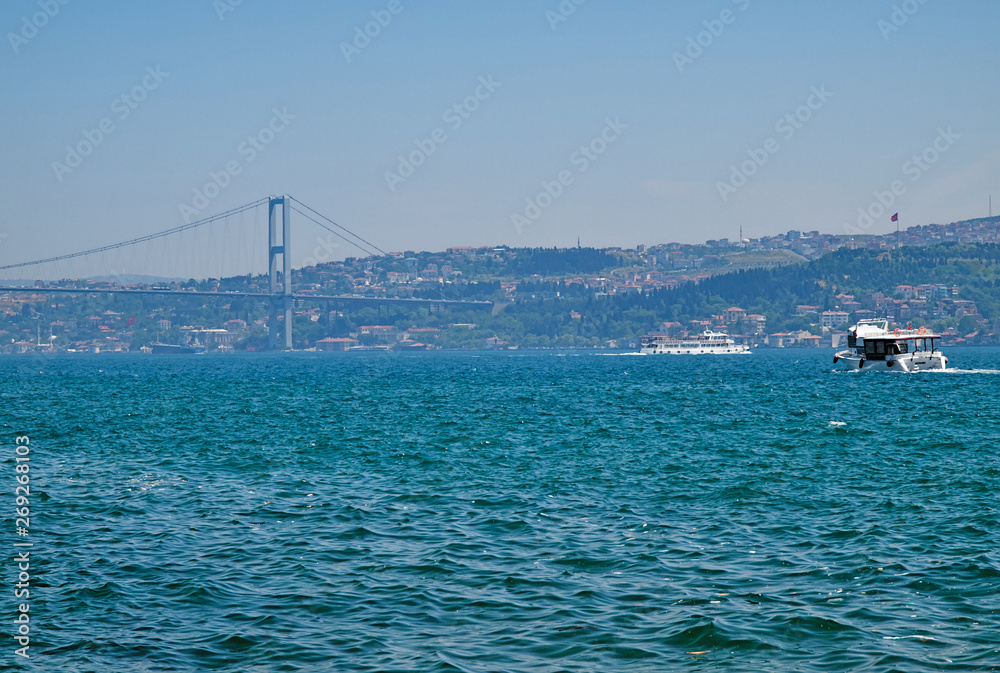 View to Bosporus strait second bridge (Fatih Sultan Mehmet Bridge) and a cruise boat on a summer day, Istanbul, Turkey.