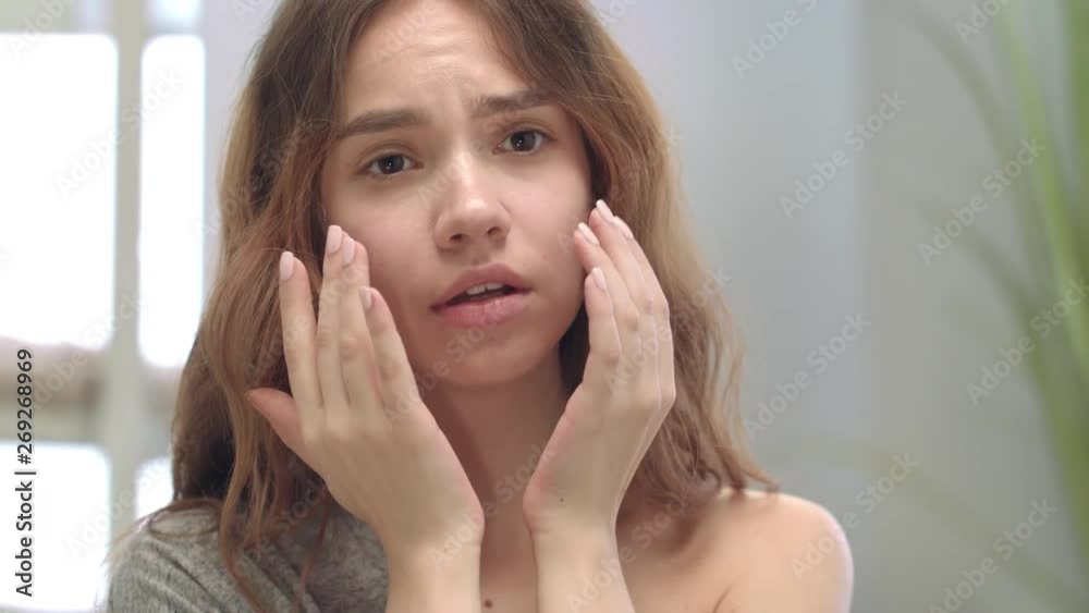 Dissatisfied woman touching face skin in bathroom mirror. Problem skin concept Dissatisfied woman touching face skin in bathroom mirror. Problem skin concept