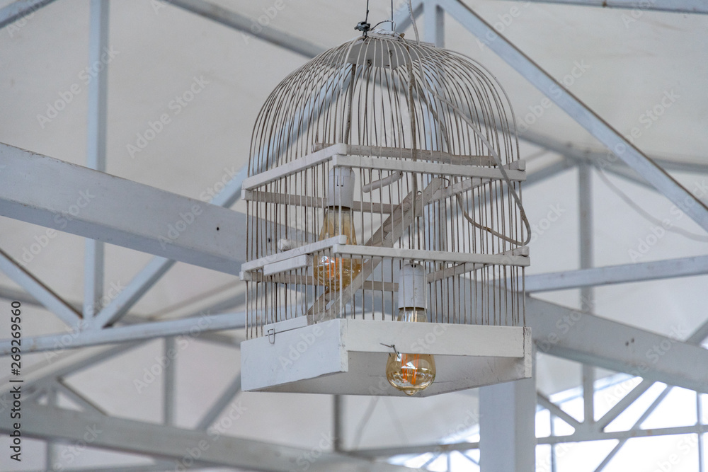 Obraz premium Two Edison light bulbs inside lampshade made from white painted wood bird cage. Closeup of birdcage reused into ceiling lamp with golden glass lightbulb inside. Stripes and geometric textures