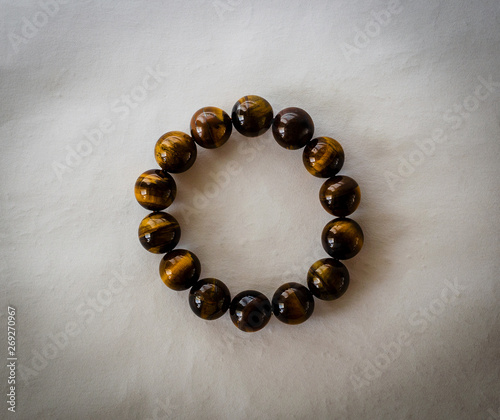 The jewelry is a bracelet made of round stones of tiger eye. Perfectly polished to shine with the reflection of light on the edges. On white vintage background with shadows.