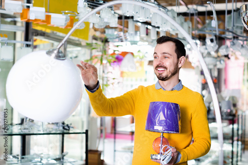 Man in shop of home appliances choosing modern and stylish lamp