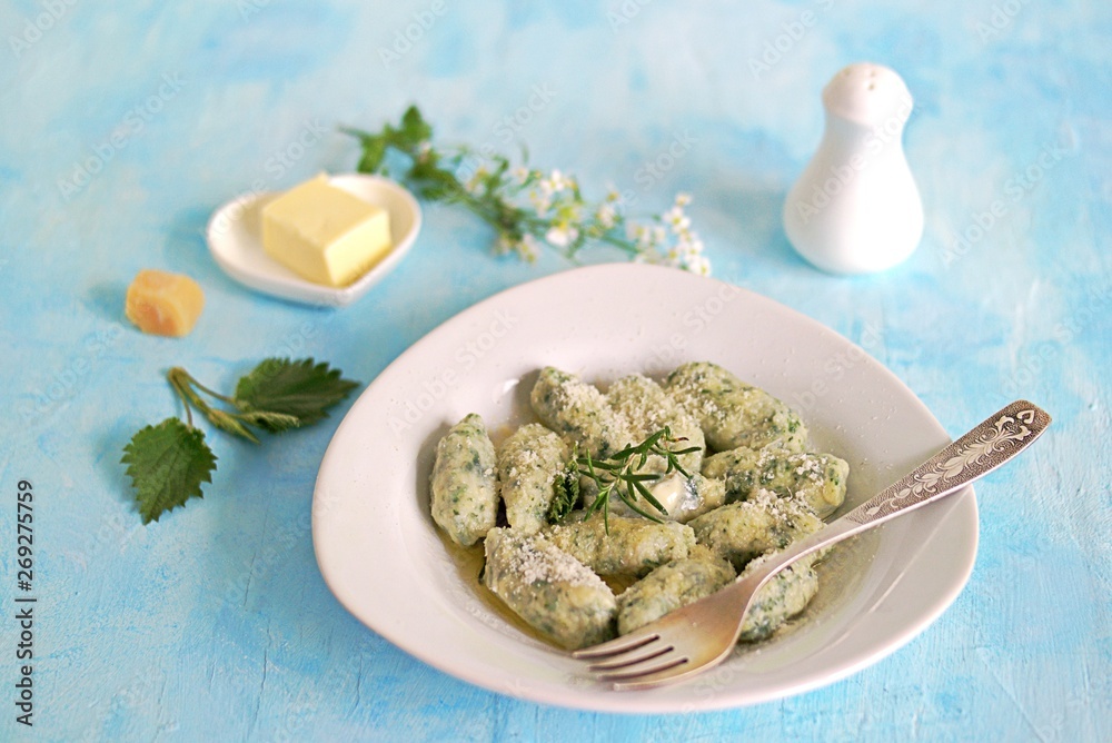 Gnocchi or dumplings with nettle or spinach on a white plate on a light blue background. Served with butter and parmesan cheese. Italian food. Selective focus Gnocchi or dumplings with nettle or spinach on a white plate on a light blue background. Served with butter and parmesan cheese. Italian food. Selective focus
