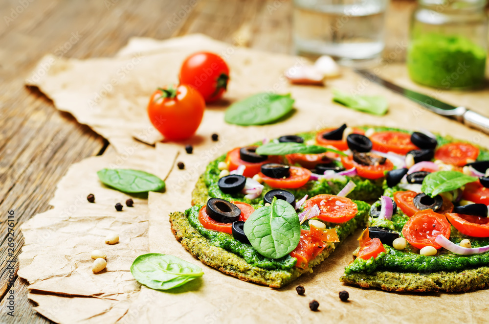 vegan broccoli zucchini pizza crust with spinach pesto, tomatoes, onion and olives