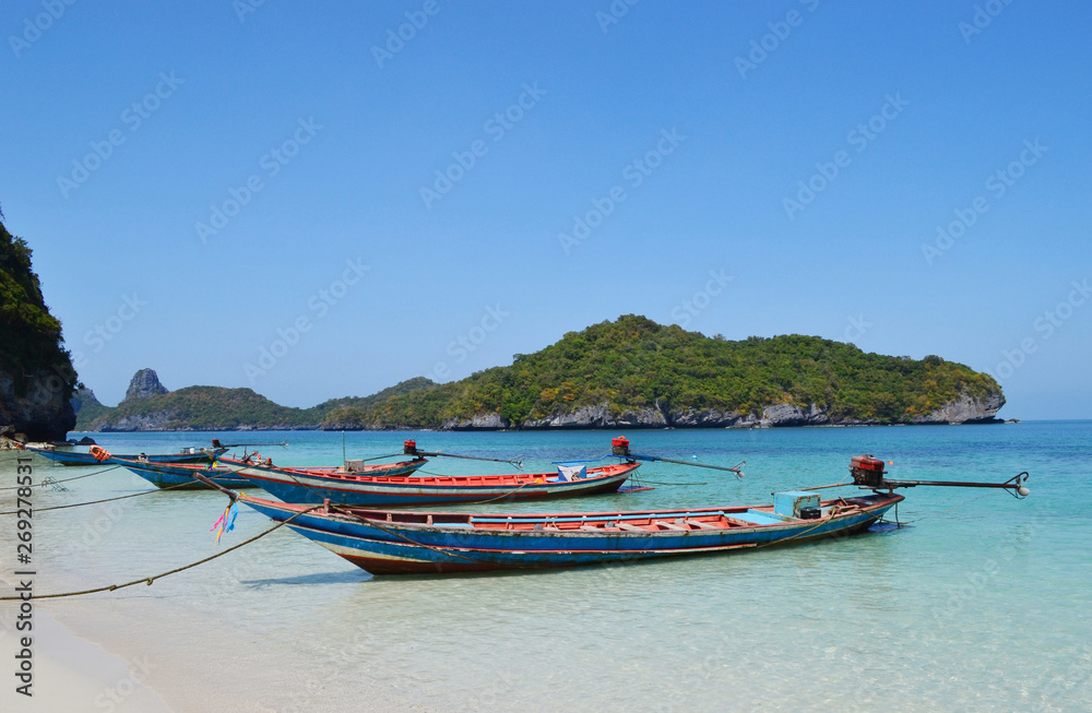 Boats near the beach in Ang Thong National Park on the background of an island with trees and blue sky and sea.