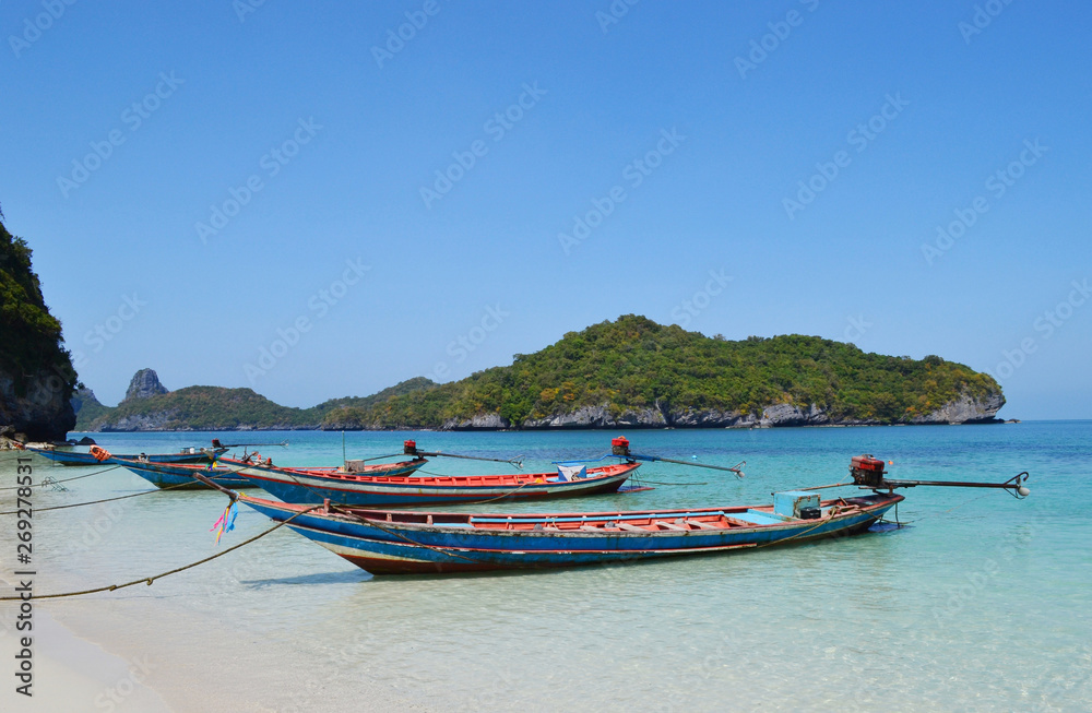 Boats near the beach in Ang Thong National Park on the background of an island with trees and blue sky and sea. Boats near the beach in Ang Thong National Park on the background of an island with trees and blue sky and sea.