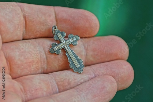  small gray silver cross is lying on the fingers