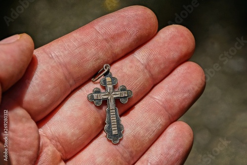 gray silver cross is lying on the fingers