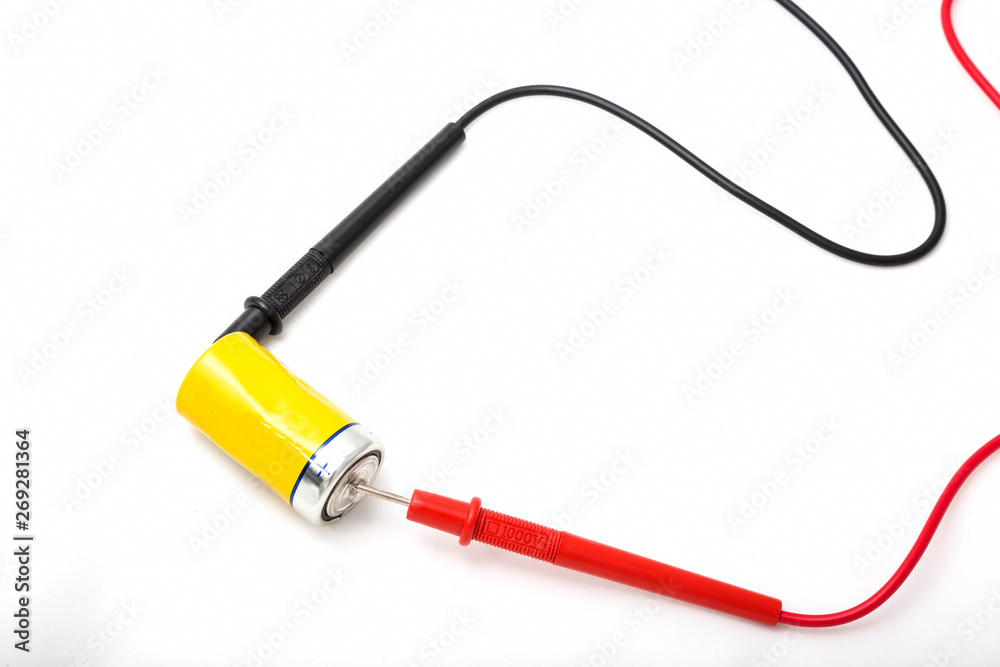 Fototapeta premium Multimeter wires and yellow battery. Checking battery voltage. Red to plus. Close up, isolated on white background