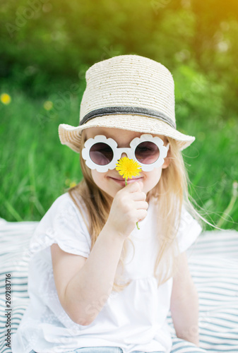 Happy little girl sitting on the green grass with flower dandelion in your hands, summer concept, funny sunglasses