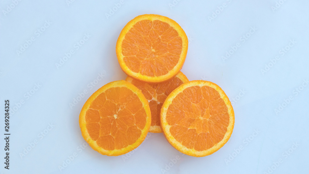 Four orange slices lay on a white background with one slice in the middle laying under the remaining three resting on top of it creating beautiful food art. Four orange slices lay on a white background with one slice in the middle laying under the remaining three resting on top of it creating beautiful food art.