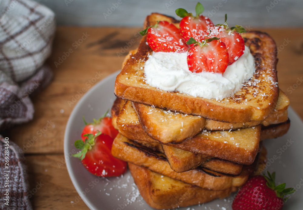 Close-up of french toast with fresh strawberries, coconut shreds and honey, on wooden background Close-up of french toast with fresh strawberries, coconut shreds and honey, on wooden background