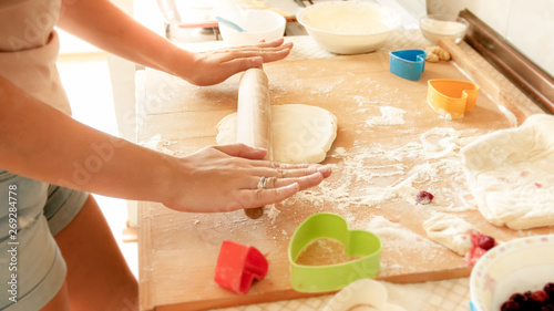 Fototapeta Naklejka Na Ścianę i Meble -  Closeup image of young woman rolling dough with wooden rolling pin. Housewife making pizza at home on kitchen