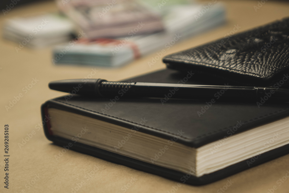 A black notebook , a pen and dollar cash banknotes on wooden background - concept of financial management or planning, make money from freelance writing A black notebook , a pen and dollar cash banknotes on wooden background - concept of financial management or planning, make money from freelance writing