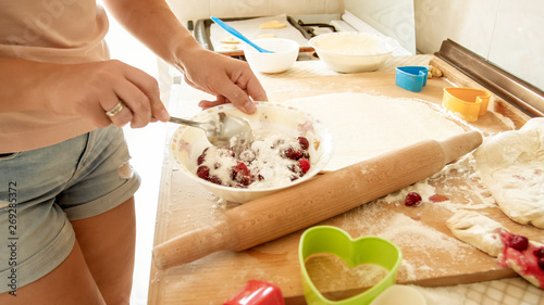 Closeup image of young housewife pouring sugar in big bowl with fgresh berries while making sauce for pie
